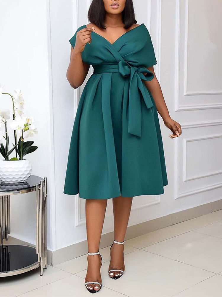 Woman wearing a dark green A-line midi dress with a V-neck wrap bodice and a self-tie sash.