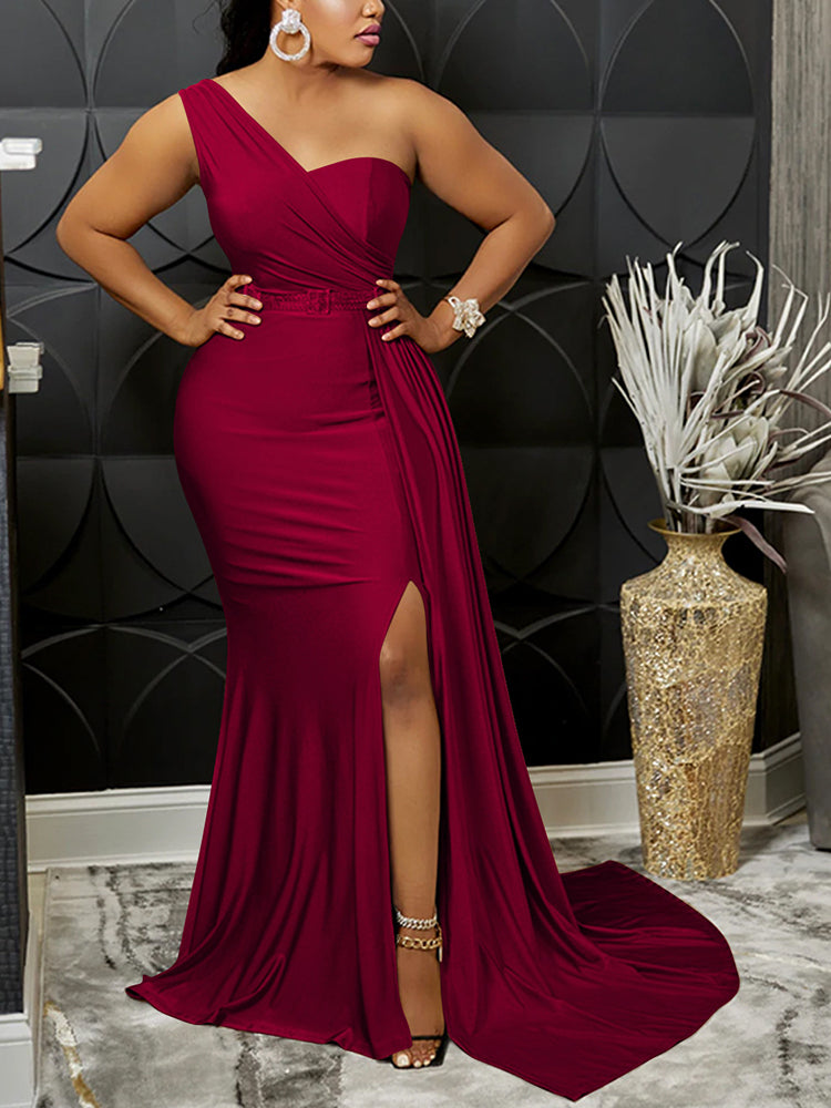 Woman wearing a burgundy one-shoulder formal gown with a thigh-high slit and mermaid hemline, standing with hands on hips.