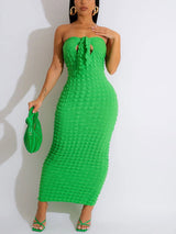 Woman wearing a strapless green midi dress with textured fabric and ruched detailing at the bust, holding a green clutch bag and wearing green strappy heels.