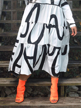 A woman wearing a white midi dress with a bold black graphic print and orange peep-toe boots, focusing on the lower half of the outfit.