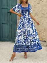 Woman wearing a blue and white floral print maxi dress with puff sleeves and a square neckline, standing outdoors.