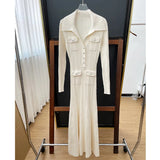 A cream-colored long-sleeved knit dress with a collared neckline, button-up front, dual chest pockets, and a flared hem, displayed on a hanger.
