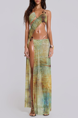 Woman wearing a green and brown abstract print halter neck maxi dress with a high slit and cut-out details.