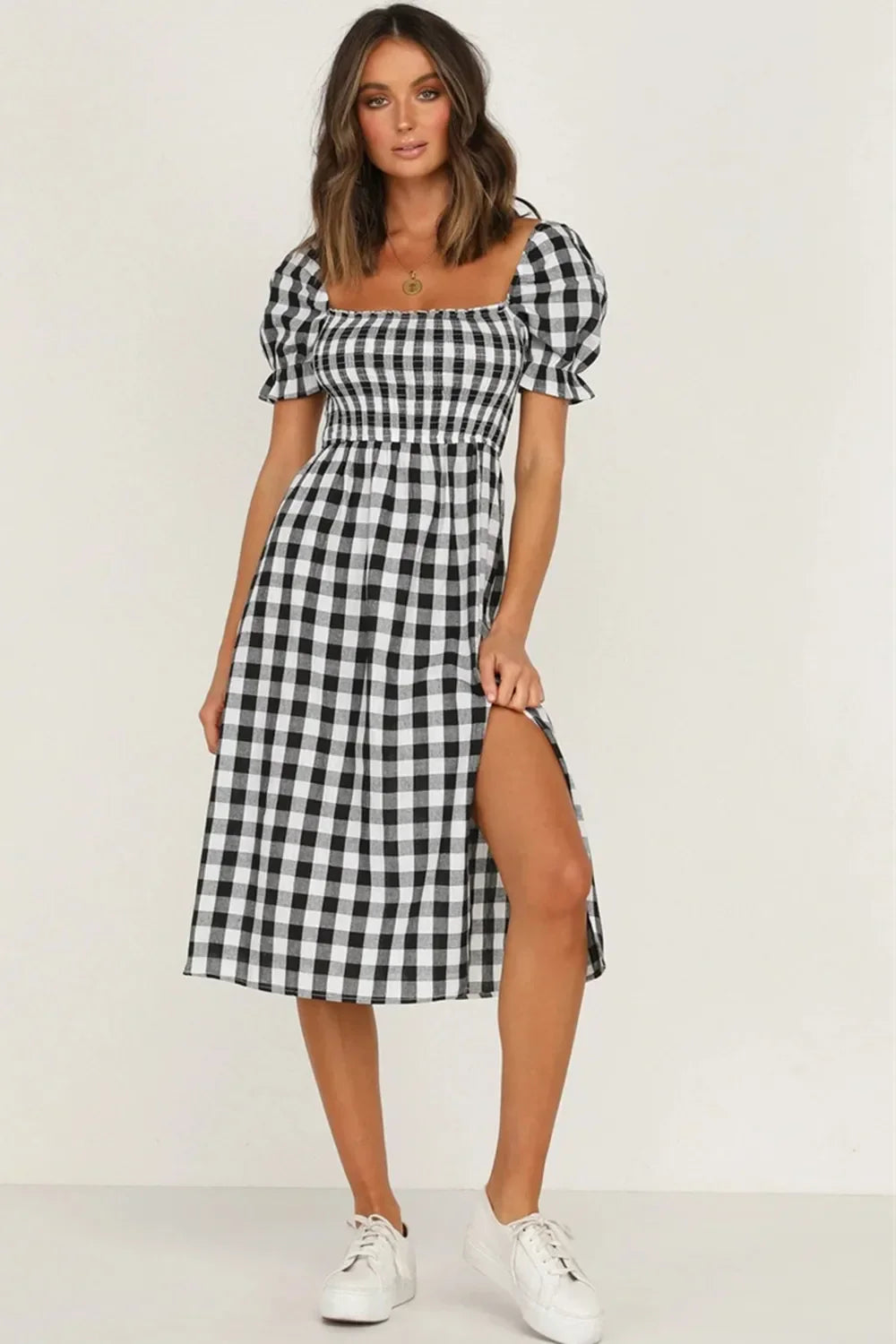 Woman wearing a black and white gingham check midi dress with puff sleeves and a square neckline, showing the thigh-high slit.