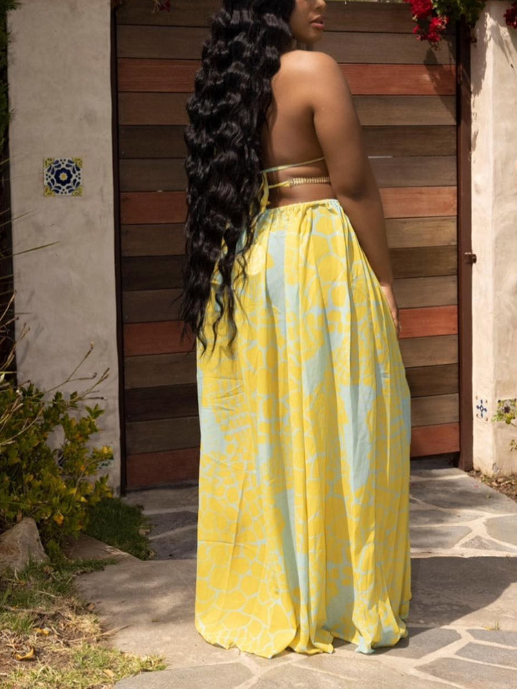Back view of a woman in a yellow and blue patterned maxi dress, highlighting the flowing skirt and back detail.