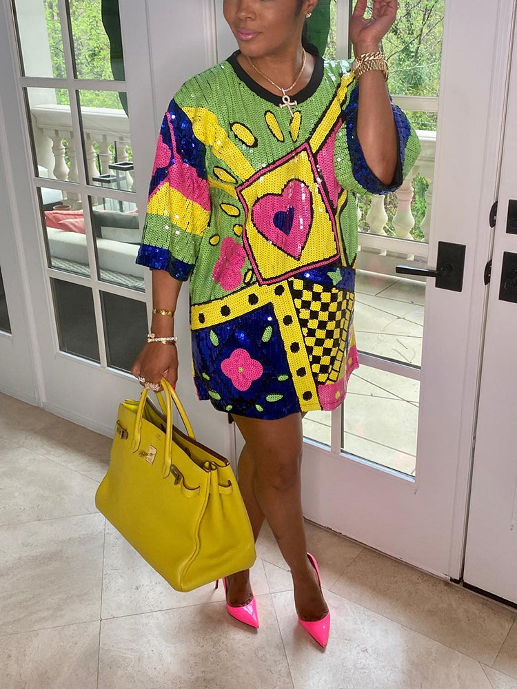 Side view of a woman in a vibrant sequined t-shirt dress with geometric and graphic details, accessorized with a yellow handbag and pink heels.