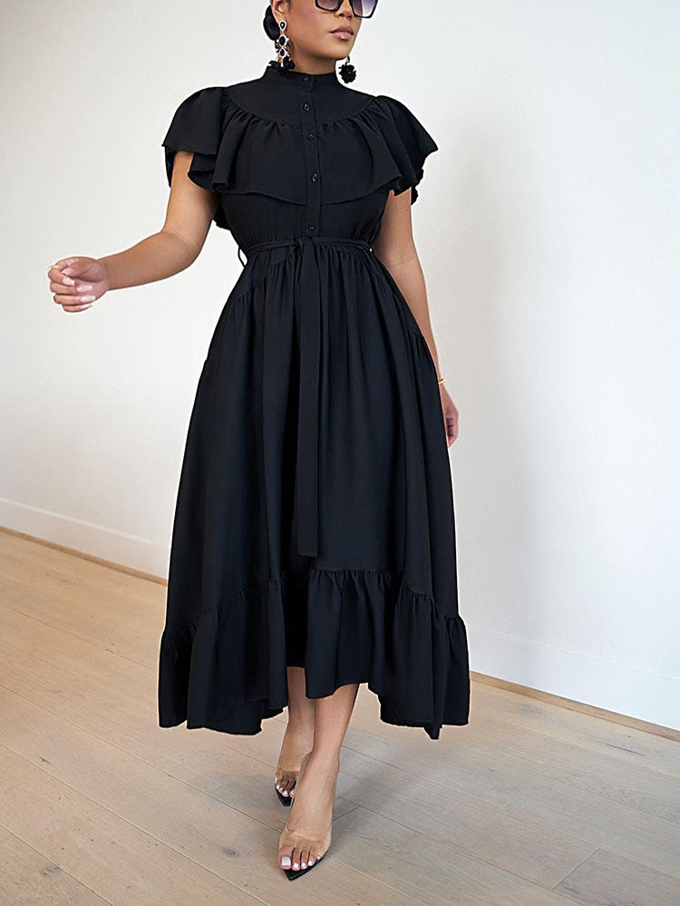 Woman in a black ruffled midi dress and clear heels, with one hand extended.