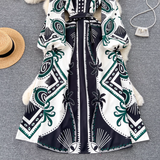 Overhead view of a bohemian print maxi dress with balloon sleeves and a high neckline, displayed with a straw hat and a small pearl handbag.