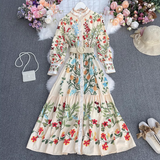 Cream floral print maxi dress with long sleeves and a belted waist, laid flat on a grey background with decorative flowers and accessories.