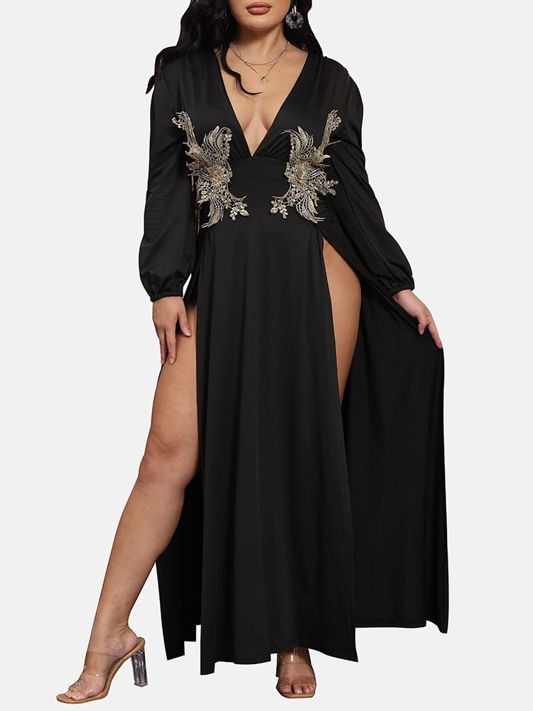 Full view of a woman in a black evening gown with long sleeves and two high leg slits.