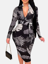 Woman in a black midi dress with a grey and white leaf print, V-neck, long sleeves, and a belted waist.