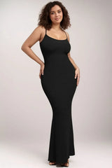 Woman in a long black ribbed knit dress with thin straps, hands on hips.