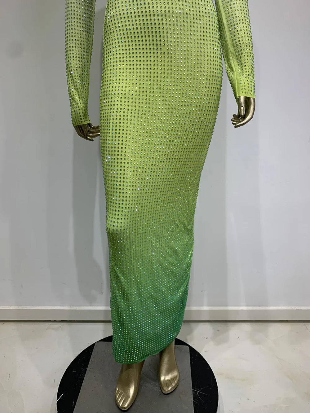 Close-up of the lower portion of a gradient green, rhinestone-embellished dress on a mannequin.