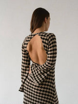 Back view of a woman wearing a long-sleeved knit dress with an open back and a black and beige geometric diamond pattern.