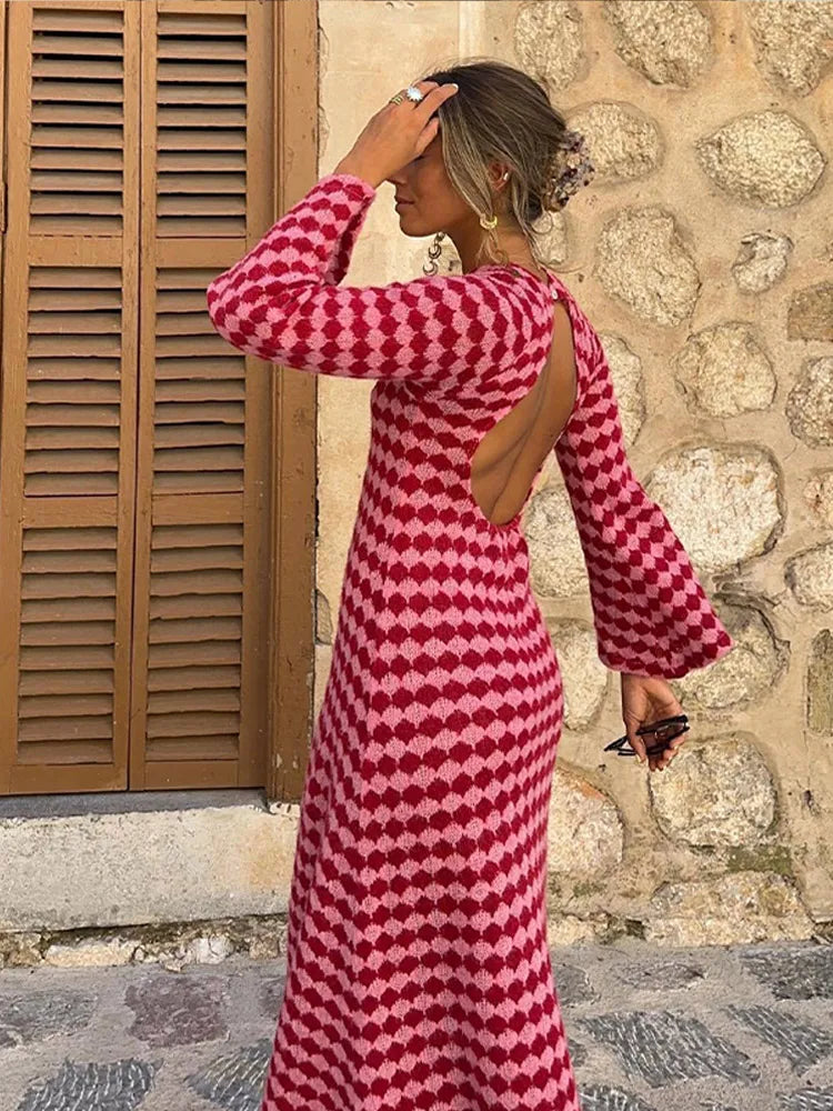Woman wearing a long-sleeved, midi-length knit dress with an open back and a pink and red geometric diamond pattern.
