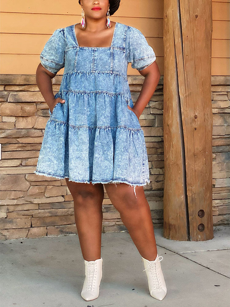 woman wearing a blue denim tiered babydoll dress with puff sleeves and a square neckline, accessorized with floral print lace-up platform heels and a round woven bag