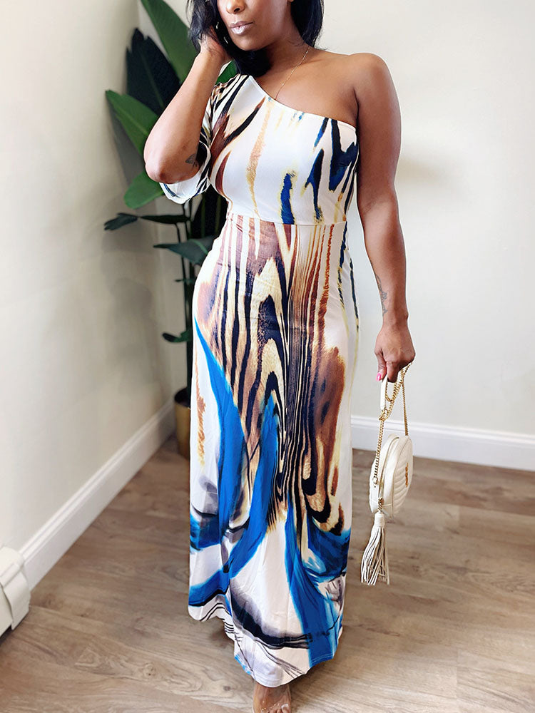 Woman wearing a one-shoulder maxi dress with an abstract print, holding a white handbag.