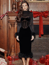 Woman in a black velvet dress with sheer sleeves and feather trim posing in a festive setting