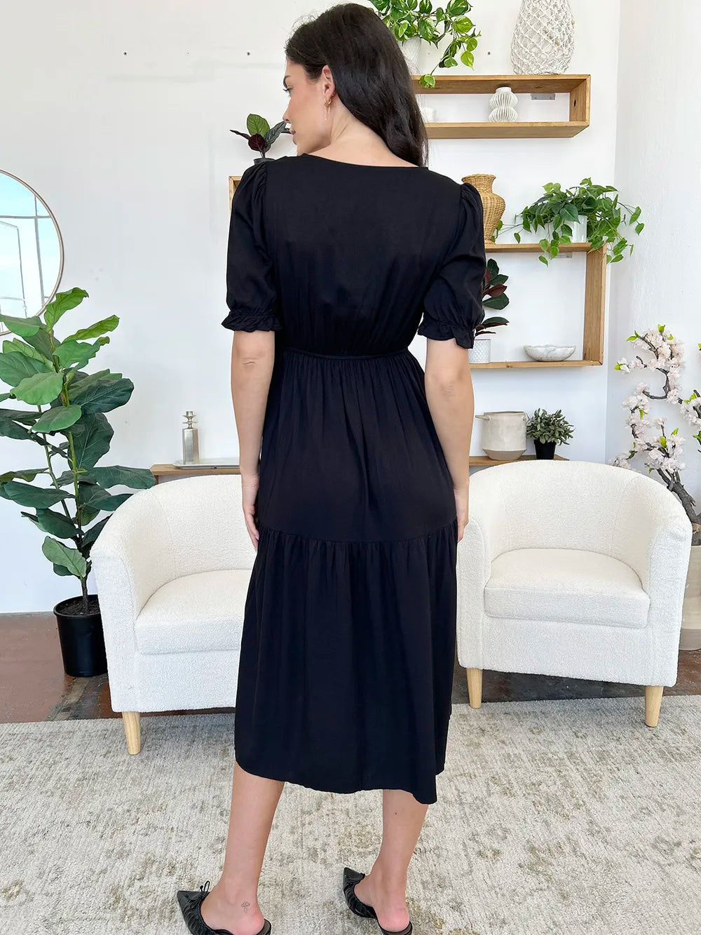 Back view of a woman in a black midi dress with short sleeves and a tiered skirt.