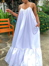 Woman wearing a flowing white maxi dress with ruffled hem and spaghetti straps, standing outdoors.