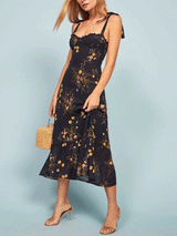 Full body shot of a woman in a black floral print midi dress, holding a straw handbag.