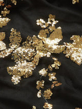 Close-up of the gold sequined floral appliqué on the black mesh fabric of the dress