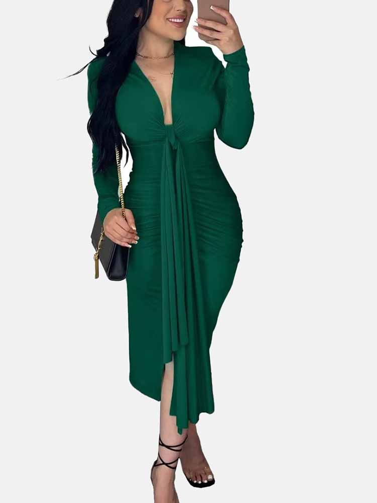 Woman wearing a long-sleeved green ruched dress with a tie-front detail and a slit hem, holding a black purse.