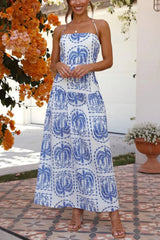 Woman wearing a white maxi dress with a blue palm tree print and halter neckline, standing outdoors