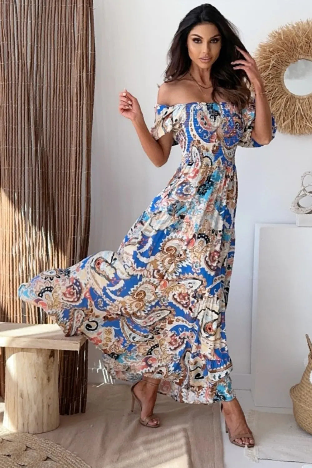 Woman twirling in a flowing paisley print off-the-shoulder maxi dress.