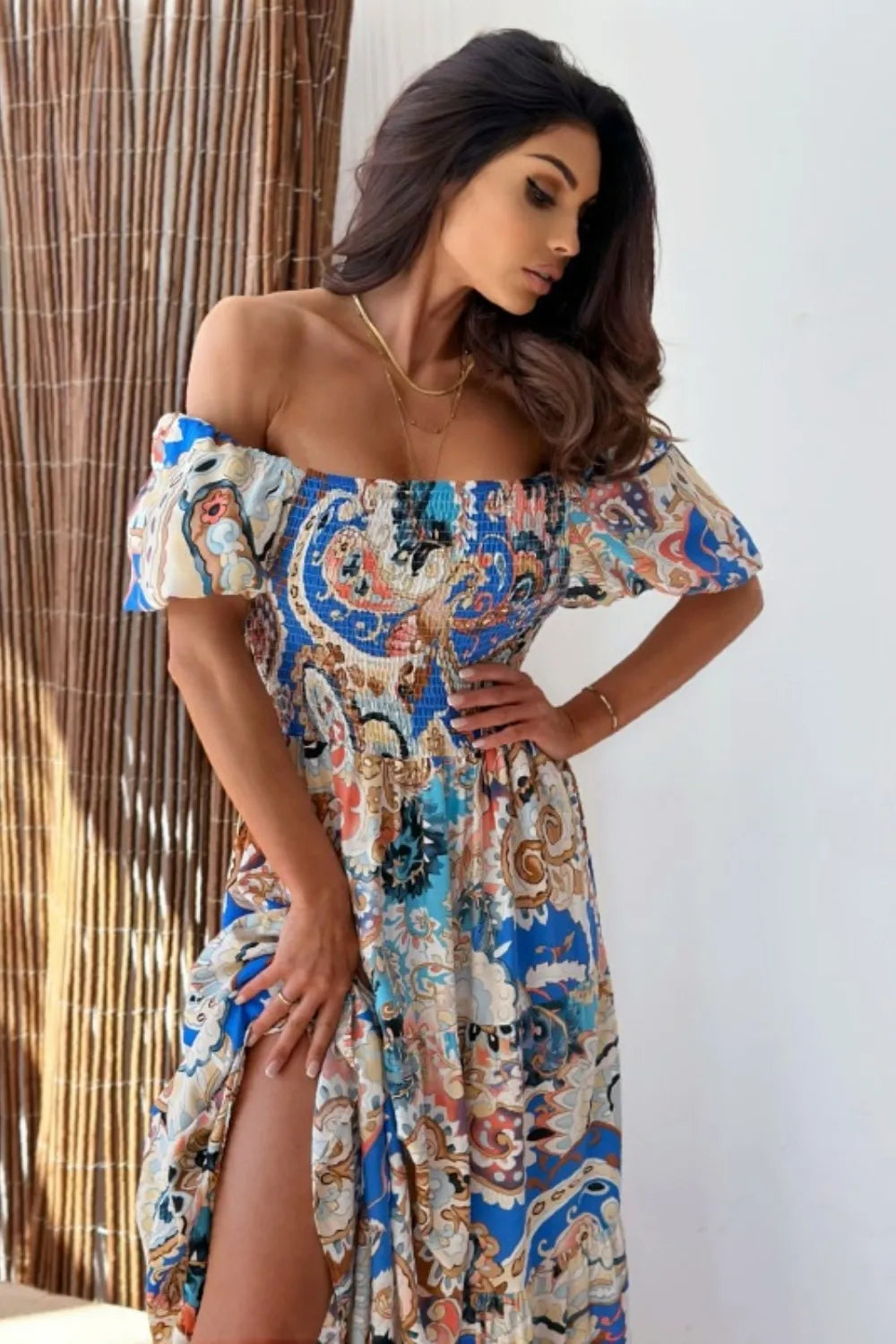 Woman wearing a blue and white paisley print off-the-shoulder maxi dress with a high slit.