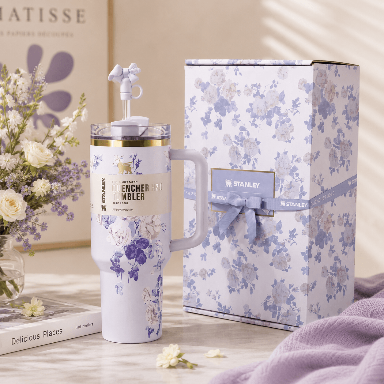 Floral-patterned tumbler with matching gift box on a wooden surface with flowers and books in the background.
