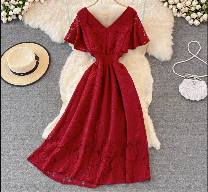 Red lace dress with V-neck and flutter sleeves displayed on a white fluffy rug, with a straw hat and a white beaded purse nearby.