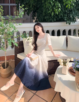 Woman wearing a white and dark blue ombre gradient fit and flare midi dress with puff sleeves, sitting on a couch outdoors.