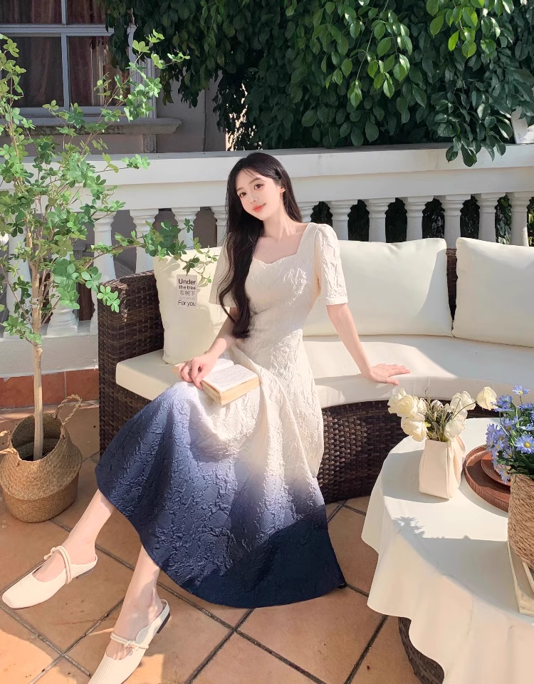 Woman wearing a white and dark blue ombre gradient fit and flare midi dress with puff sleeves, sitting on a couch outdoors.