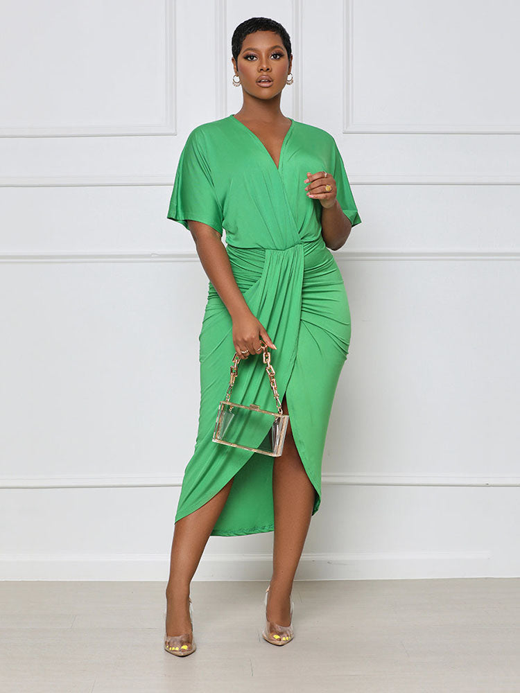 Woman wearing a green V-neck, short-sleeve, ruched, draped midi dress with a tulip hem, holding a clear handbag.
