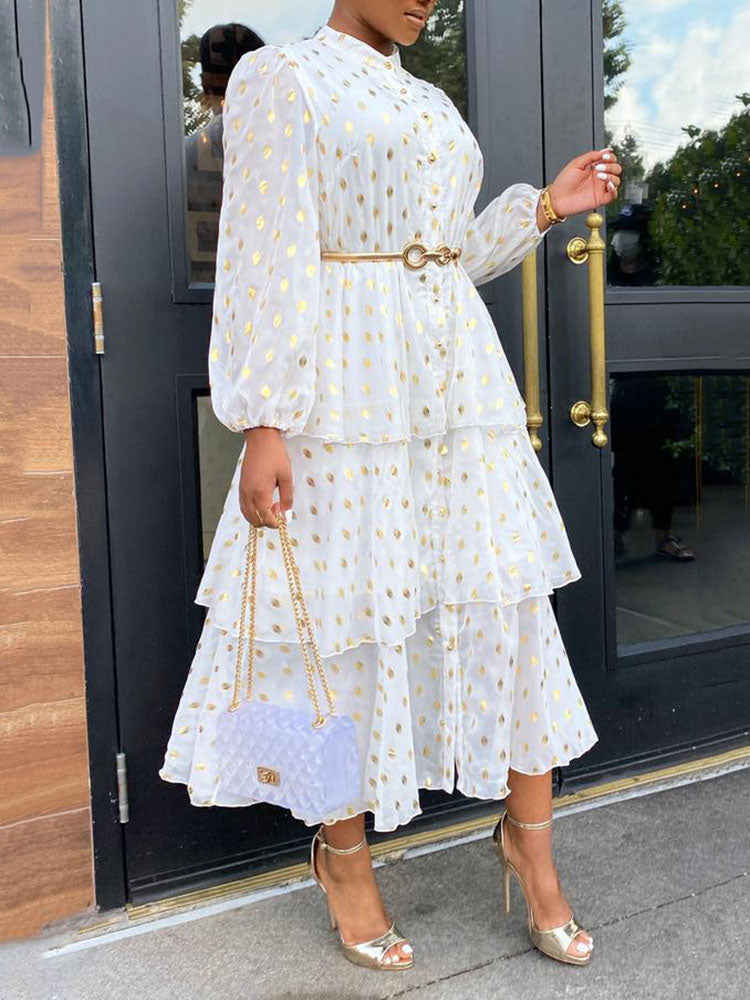 Close-up of a woman wearing a white tiered midi dress with gold polka dots and a gold belt.