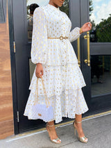 Close-up of a woman wearing a white tiered midi dress with gold polka dots and a gold belt.