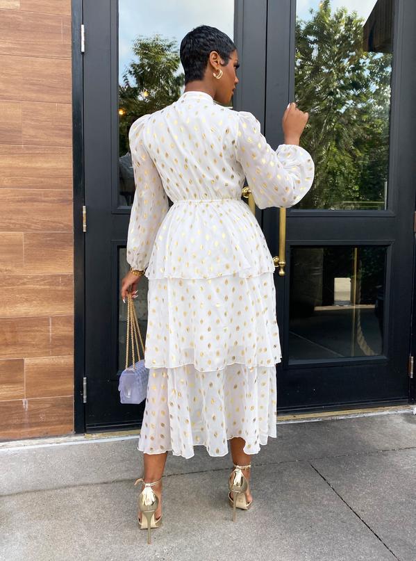 Back view of a woman wearing a white tiered midi dress with gold polka dots.