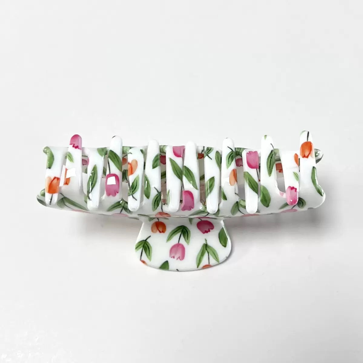 Side view of a white claw clip with a pink and orange tulip floral print, showing the teeth