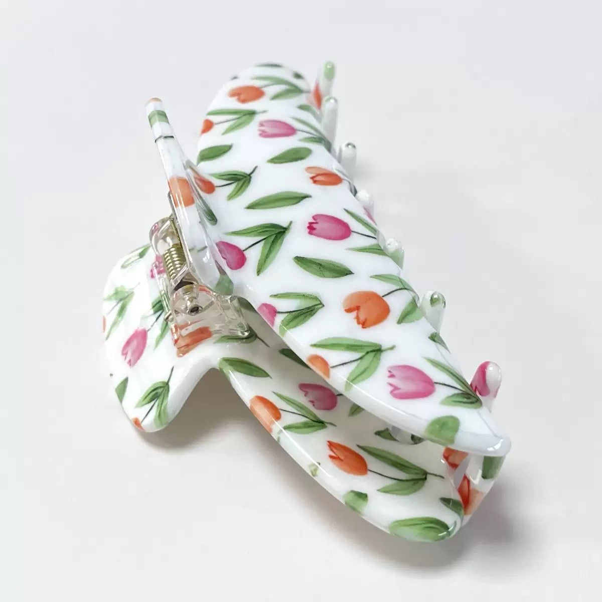 Close-up of a white claw clip with a pink and orange tulip floral print, showing the hinge mechanism