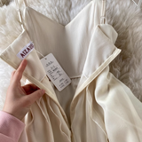 Hand holding the zipper of a cream-colored chiffon dress, revealing the interior label.