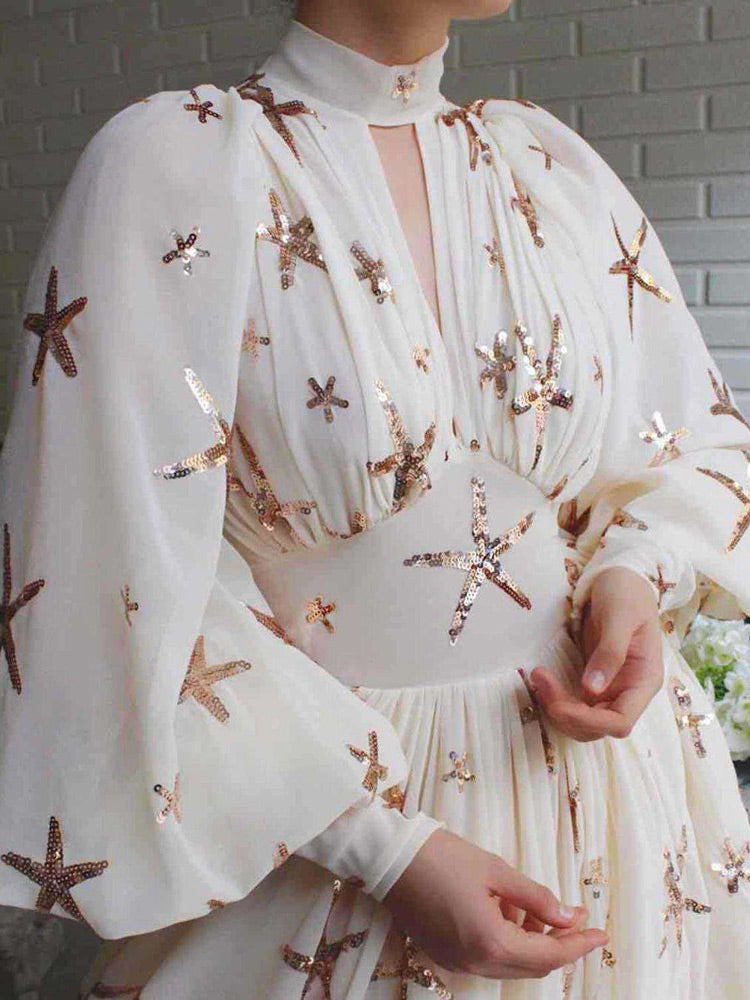 Detail of the neckline and sleeves of a white chiffon gown with starfish sequin embellishments.