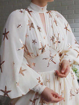 Detail of the neckline and sleeves of a white chiffon gown with starfish sequin embellishments.