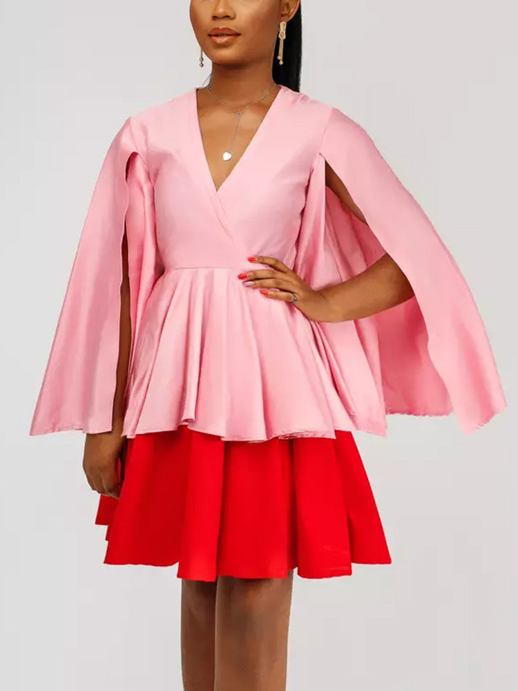Close-up of a woman's upper body in a pink and red color-block dress with cape sleeves, showcasing a necklace.