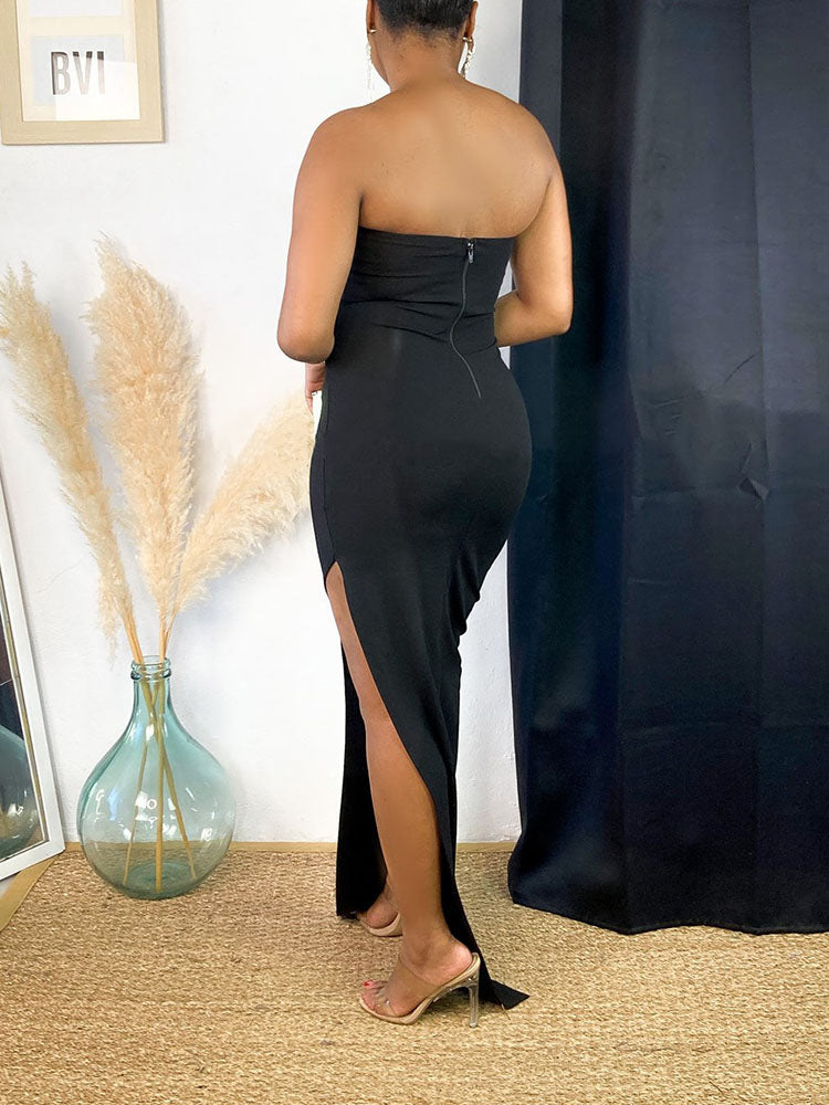 Close-up side profile of a woman in a black strapless evening gown with a high slit and embellished neckline.