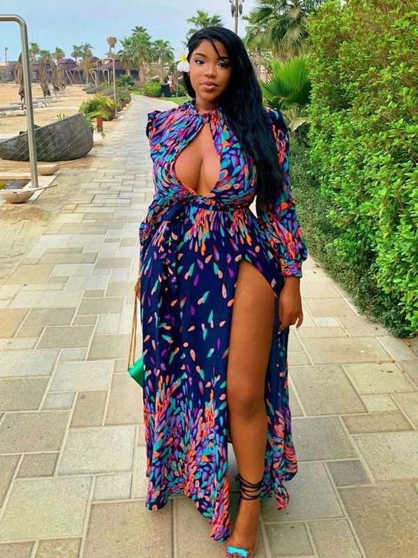 Woman walking in a long, navy blue maxi dress with a colorful abstract print, high neckline, deep V-cutout, long sleeves, and a high slit.