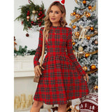Woman wearing a red plaid long-sleeve fit and flare dress with a round neck, standing in front of a decorated Christmas tree.