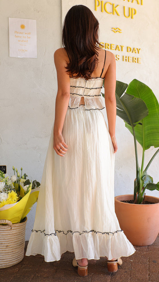 Back view of a woman wearing a white crinkle fabric two-piece set with black trim and tie details.