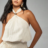 Detail of the halter neckline of a cream mini dress with a gold ring accent.