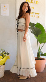 Side view of a woman in a white crinkle fabric two-piece set with black trim and tie details.